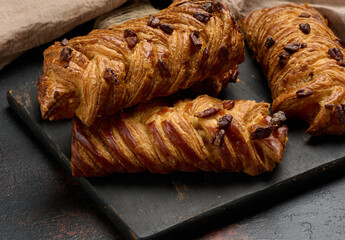 Three golden brown maple pecan braid pastries are arranged on a dark, textured surface. Braided...