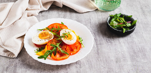 Light appetizer of tomatoes, boiled egg, cheese and arugula on a plate web banner