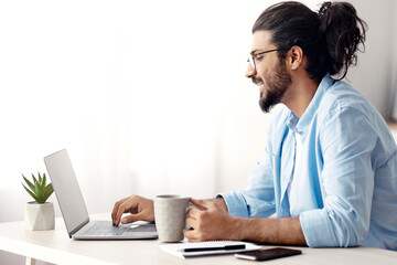 Remote Work. Handsome Male Freelancer Using Laptop And Drinking Coffee, Working Remotely At Home...