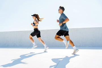 Two Athletes Sprinting Energetically Under a Clear Blue Sky During a Sunny Day at a Modern Urban...
