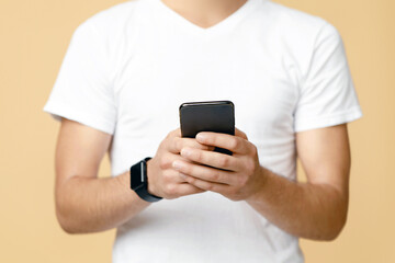 Social networks, blogs and mobile app. Smiling handsome young blogger student in white t-shirt with smart watch in glasses hold phone and surfing in internet isolated on light background, cropped