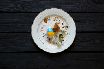Easter meal leftovers and an egg with the Ukrainian flag, Easter cake crumbs and a branch of cherry blossoms on a white plate