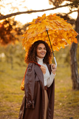 happy girl in coat standing in autumn park with beautiful umbrella made of yellow leaves