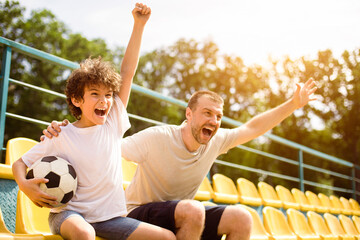 Goal. Emotional man and little boy cheering their favorite team, little boy holding soccer ball © Prostock-studio