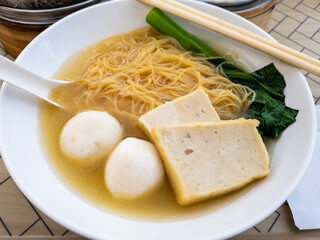 A delicious bowl of noodle soup with fish balls, fish cake slices and green vegetable.