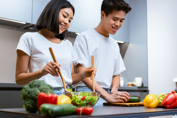 Japanese Couple Cooking Salad In Kitchen, Husband Helping Wife Cook Healthy Dinner At Home. Asian Family Cooks Together Enjoying Meal Preparation. Nutrition And Food Recipe. Selective Focus