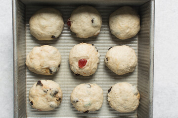 Overhead view of hot cross bun dough rising in a silver baking pan, top view of bun dough rolled into balls in a baking tin, process of making hot cross buns