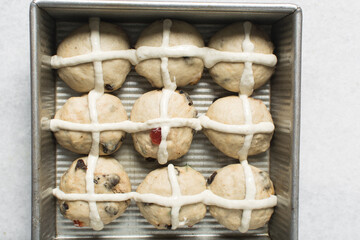 Overhead view of hot cross bun dough rising in a silver baking pan, top view of bun dough rolled into balls in a baking tin, process of making hot cross buns