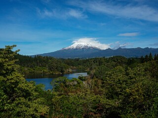 Panoramic view of the iconic snow capped Mount Taranaki Egmont National Park from lush green bush forest at Lake Mangamahoe New Plymouth New Zealand