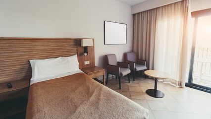 Modern hotel room interior with single bed, wooden headboard, nightstand, two armchairs, round coffee table, curtain-covered window and balcony door with sunlight; wide-angle indoor shot, Punta Umbria
