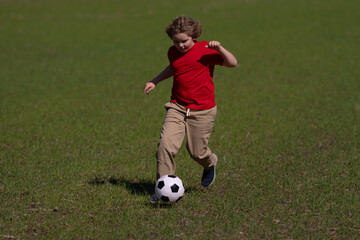 Obraz premium A kid is playing soccer in the park. A child kicks the soccer ball. The kids sport. Kid football player runs toward the goal. Kid kicking the soccer ball. A sporty child. Kids are playing soccer on