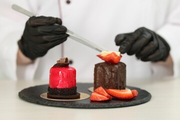 Confectioner decorating tasty dessert at white wooden table in kitchen, selective focus