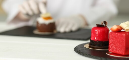 Confectioner decorating tasty dessert at white wooden table in kitchen, selective focus