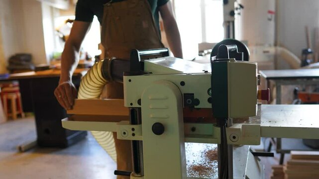 Unrecognizable carpenter prepares jointer machine for woodworking. Tool for cleaner planing, minimizing chipping at knots, thickness machine for joinery, plane wood bars and handmade business, hobby