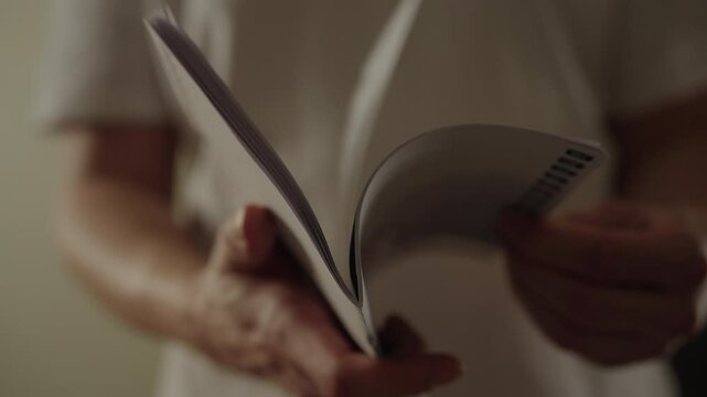 Close-up view of male hands turning pages of instruction manual, engaging in reading and absorbing new information. Repairman leafing through instruction manual, studying details indoors, slow motion.