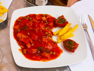 Healthy dinner of tilapia fillet stewed with vegetables served with side dish of french fries and sun-dried tomatoes topped with aromatic pesto sauce