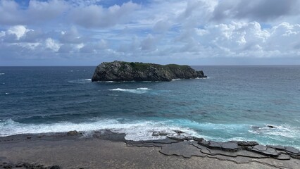 The rock formation known as Lion Island, a sea lion shaped rock. Turquoise blue sea, sky full of clouds. Sunset hour. Fernando de Noronha, Brazil, Praia do Leão.