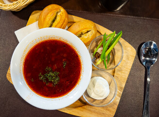 Bowl of traditional borscht garnished with dill, served with sour cream and freshly baked bread, perfect for wholesome meal. Ukrainian cuisine