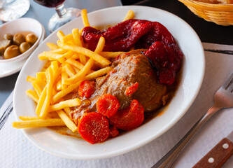 Appetizing stewed pork cheeks served with vegetable garnish of baked red bell pepper and french fries