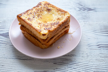 Close-up of buttered french toast with syrup and honey on pink plate