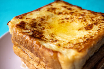 Close-up of buttered french toast with syrup and honey on pink plate