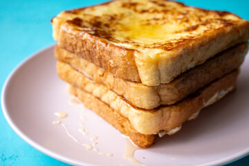 Close-up of buttered french toast with syrup and honey on pink plate