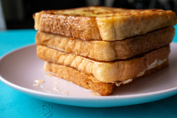 Close-up of buttered french toast with syrup and honey on pink plate