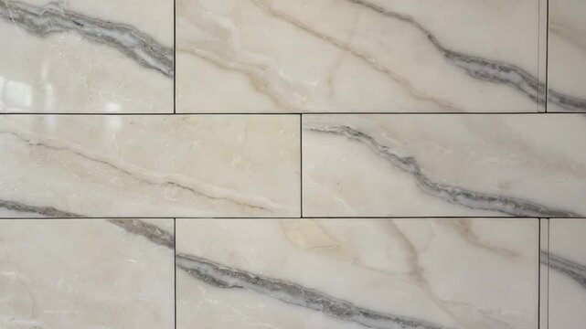 Close up of smooth white and beige marble stone tiles with light gray veining and dark grout lines arranged horizontally