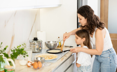 Girl is naughty while cooking pancakes with her mother. Woman and girl fry pastry dessert in frying...