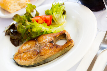 Tasty broiled steak of bonito served with vegetable salad on white plate..