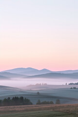 Obraz premium Pastel Sky Over Misty Landscape: Rolling hills fade into dawn's soft hues, veiled by ethereal mist, in a tranquil sunrise vista.