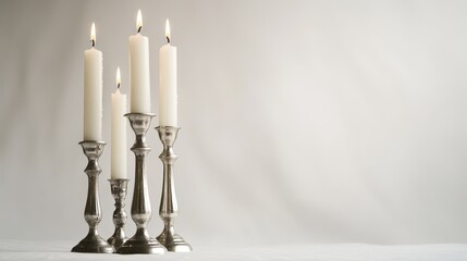 Three tall candlesticks hold white candles against a white backdrop.  Space is available for writing.
