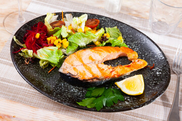 Delicious healthy dinner of baked salmon steak served with lemon slice and fresh vegetable salad..