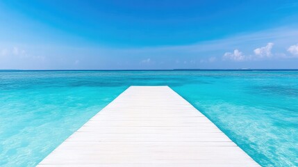 Fototapeta premium White wooden pier extending into the calm turquoise tropical ocean under a clear blue sky.