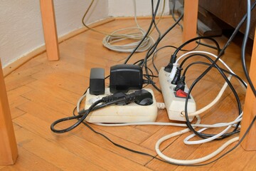 Cable chaos clutter from multiple electric wire extension cords and multi-contact plugs on wooden...