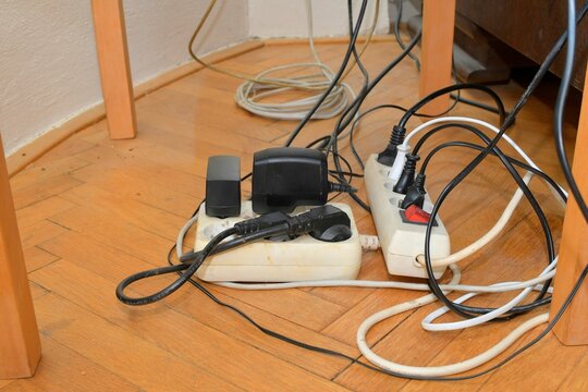 Cable chaos clutter from multiple electric wire extension cords and multi-contact plugs on wooden floor. Tangled cables on the parquet floor.