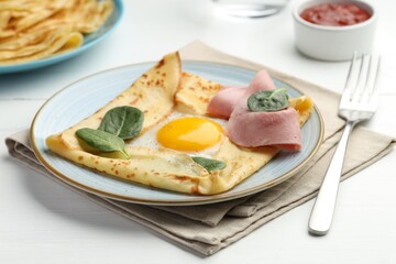Delicious crepe with egg, ham and basil on white wooden table, closeup