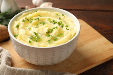 Tasty mashed potato with green onion in bowl on wooden table, closeup