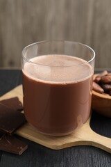 Tasty chocolate milk, bars and cocoa beans on black wooden table, closeup