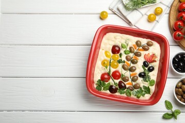 Raw focaccia with vegetables, olives and spices on white wooden table, flat lay. Space for text