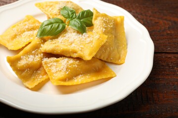 Delicious ravioli with parmesan cheese and basil on wooden table, closeup