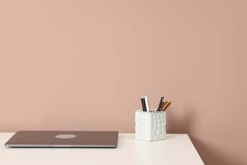 Laptop and different stationery on white office table against dark beige background