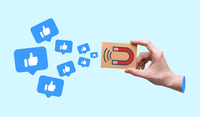 A hand holding small paper with magnet icon pulling thumb up or like icons, Followers and likes on social media, Contemporary art collage, Light blue background