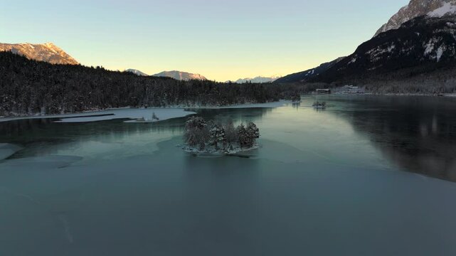 Aerial view of Ludwigsinsel, Heissenbuchel on frozen Eibsee Lake near Garmisch-Partenkirchen, Bavaria, Germany. Peaceful winter morning with snow-covered trees and icy waters creates a magical scene. 