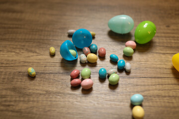 multi-colored jellybeans spilling out of a dark blue plastic Easter egg with a light blue Easter egg and a green Easter egg against a wood background