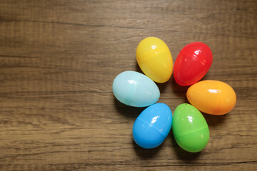 close-up flat lay of plastic red, blue, green yellow and orange Easter eggs in a circle against a wooden background with copy space 