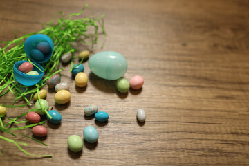 multi-colored jellybeans spilling out of the a light blue and dark blue plastic Easter eggs against a wood background with green Easter grass