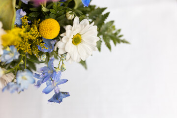 close up of a spring floral bouquet of white, blue, and yellow flowers with green leaves against a soft white background with copy space