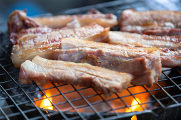 Pincers grabbing pork ribs being grilled on charcoal grill, closeup
