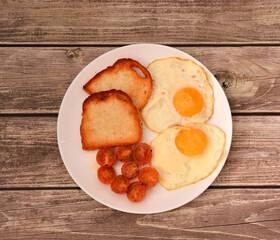 Large plate with fried eggs, wheat croutons and roasted cherry tomatoes on a wooden table.